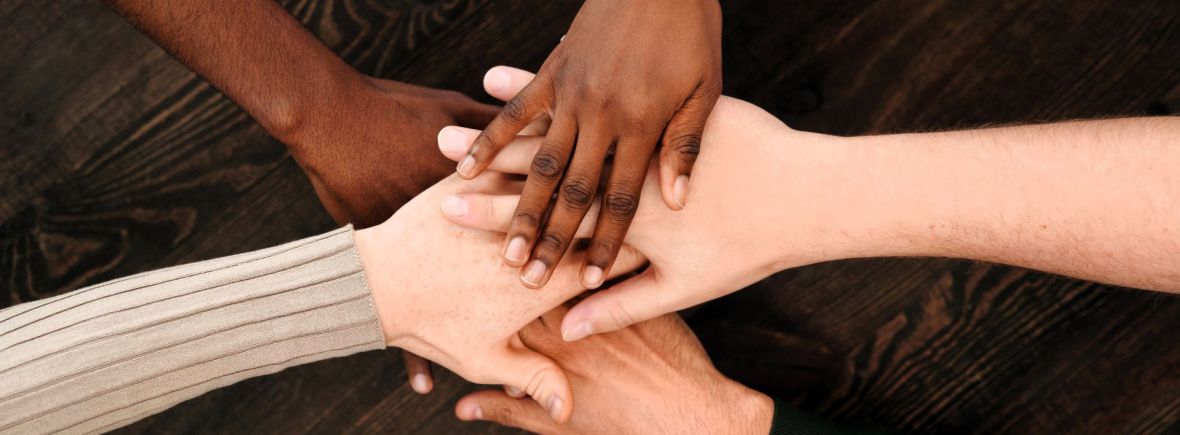 Hände unterschiedlicher Hautfarbe liegen aufeinander und symbolisieren Unterstützung, Verbundenheit und Internationalität im Kamilluskreis der Kamillianer