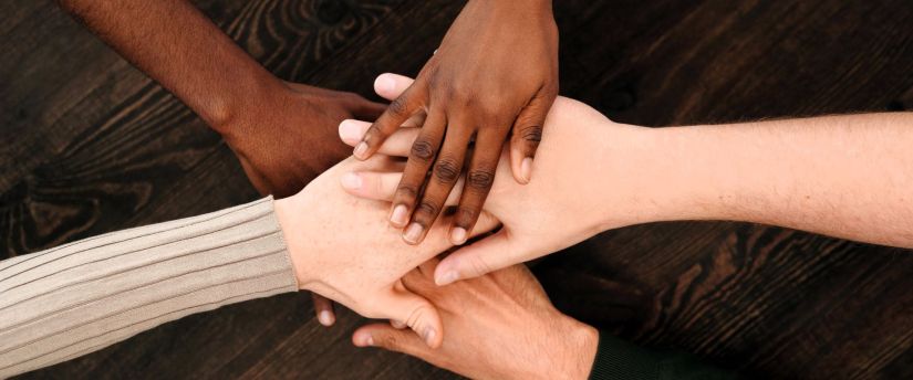 Hände unterschiedlicher Hautfarbe liegen aufeinander und symbolisieren Unterstützung, Verbundenheit und Internationalität im Kamilluskreis der Kamillianer